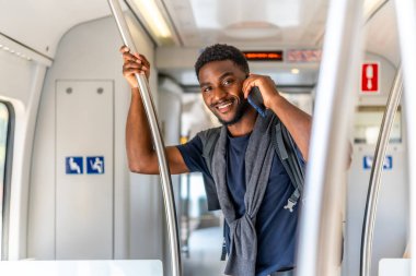 Metroyla seyahat eden cep telefonuyla konuşurken gülümseyen neşeli Afrikalı genç işadamı.
