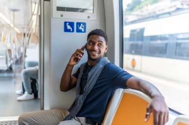 Akıllı Afrikalı iş adamı metroda oturmuş pencerenin yanında cep telefonuyla konuşuyor.