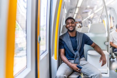 Halka açık bir metroda otururken kameraya gülümseyen yakışıklı bir Afrikalı gencin portresi.