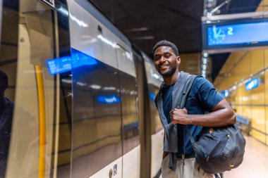 Afrikalı genç işadamı gece metro istasyonunu bekliyor. Platformda duruyor ve kameraya gülümsüyor.