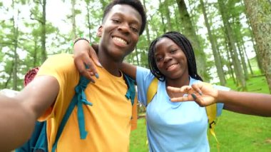Mutlu Afrikalı çift ormanda yürürken selfie çekiyor. Kucaklıyor ve el kol hareketi yapıyor.