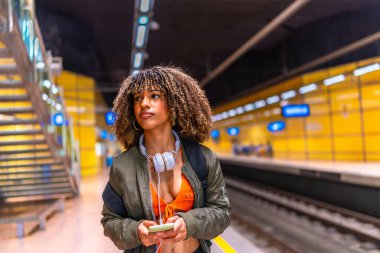 Latin güzeli genç bayan öğrenci platformda metro bekliyor ve telefon kullanıyor.