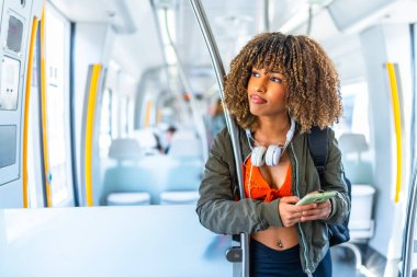 Dikkati dağınık, kıvırcık saçlı, metroda telefon kullanırken yüzünü çeviren Latin, genç bir kadın.