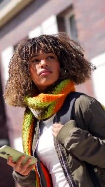 Şehirde telefon kullanan, kalın elbiseli, dikkati dağılmış Latin bir kadın.