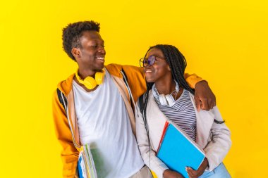 Studio portrait with yellow background of two male and female african university students and friends embracing for the back and smiling standing together clipart