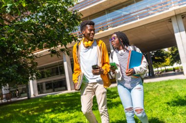 Mutlu iki erkek ve kadın Afrikalı arkadaş üniversite kampüsünde telefonla dolaşıyorlar.