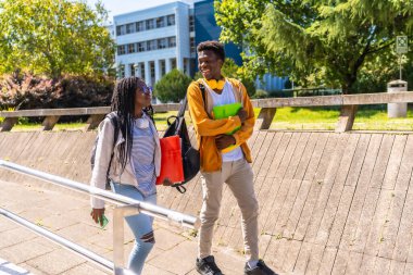 İki Afrikalı Amerikalı öğrencinin kampüs boyunca gezinip konuşmalarının yan görüntüsü.