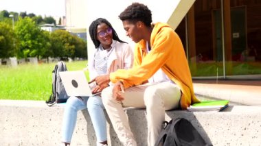 İki genç ve mutlu Afrikalı öğrenci güneşli bir günde kampüste dizüstü bilgisayar kullanıyor.