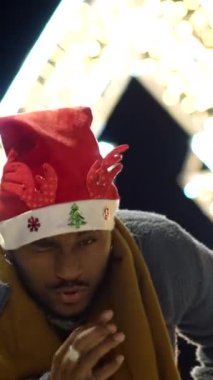 Noel Baba şapkası takan mutlu bir afro adam Noel gecesinde şehirde eğleniyor.