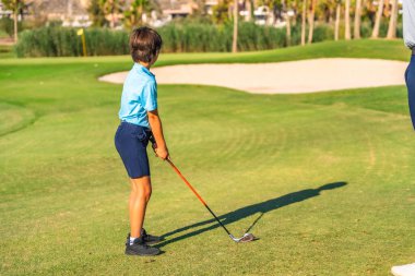 Yeşil lüks bir pistte golf oynamaya odaklanan bir çocuğun arka görüntüsü.
