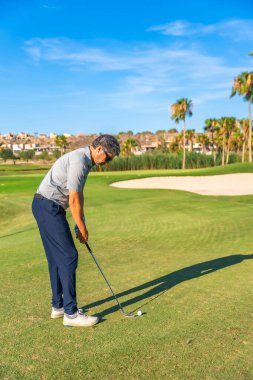 Güneş gözlüklü beyaz bir adamın dikey fotoğrafı. Güneşin altında golf oynuyor.