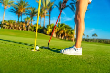 Tanımlanamayan genç bayan golfçü yeşil golf topuna vuruyor.