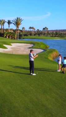 Beyaz erkek, yetişkin koç güneşin altında iki çocuğa golf oynamayı öğretiyor.