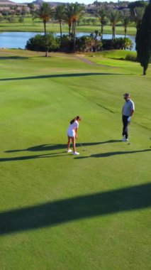 Hava aracı yazın lüks bir golf sahasında oynayan üç kişiyi geniş açıdan görüyor.