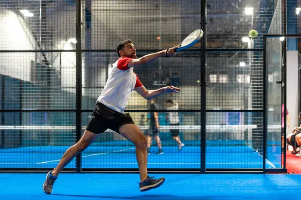 Kapalı alanda tenis oynarken topa ulaşmaya çalışan olgun bir sporcunun tam boy fotoğrafı.