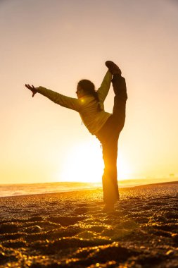 Bir kadın gün batımında plajda yoga pozu veriyor. Rahatlama ve sükunet kavramı, kadın batan güneşin sıcak, altın ışığında vücudunu gererken...