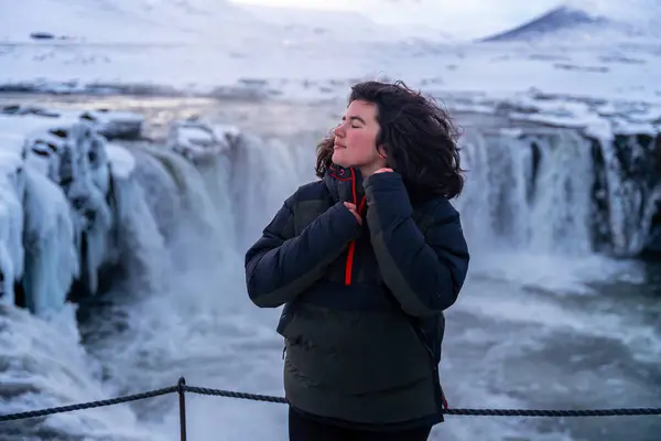 stock image Portrait of a woman at the beautiful Godafoss waterfall in winter in Iceland with her eyes closed. winter tourism