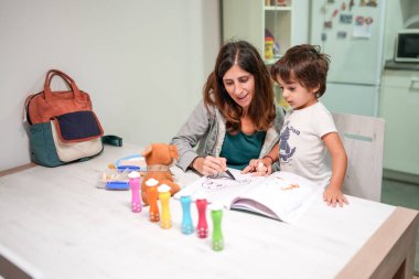 Bir kadın ve bir çocuk bir kitap ve bir çantayla masada oturuyorlar.