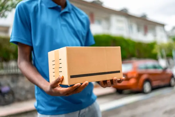 stock image Close-up of a cardboard package on hands of a delivery man on blue uniform standing on street