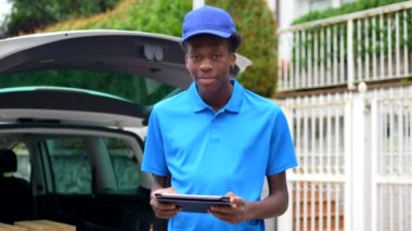 Afrikalı genç kurye, şehirde bir minibüsün yanında duran paketleri teslim etmek için dijital tablet kullanıyor.
