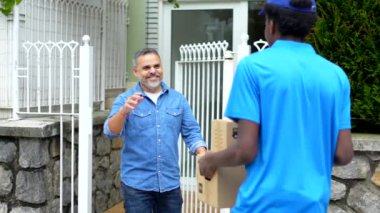 Olgun bir beyaz adam, elinde bir paket taşıyan Afrikalı bir teslimatçıya el sallıyor.