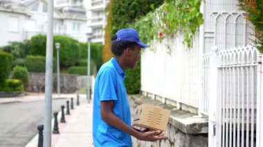 Afro-Afrikalı bir kuryenin, bir yerleşim yerinin girişinin yanında duran paketi teslim edişinin arka görüntüsü.