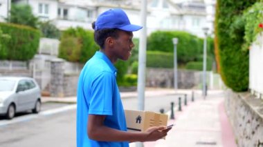 Afrikalı kurye karton paketi teslim etmek için elinde tutarken cep telefonu kullanıyor.