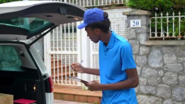 Mavi üniformalı Afrikalı kurye sokakta duran bir minibüsün paketlerini doğruluyor.