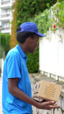 Afro-Afrikalı bir kuryenin, bir yerleşim yerinin girişinin yanında duran paketi teslim edişinin arka görüntüsü.
