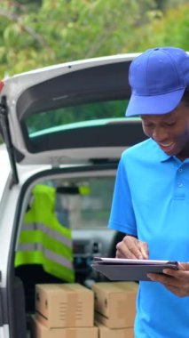 Afrikalı kurye, dijital tablet kullanıyor. Paketleri teslim etmek için minibüsün yanında duruyor.
