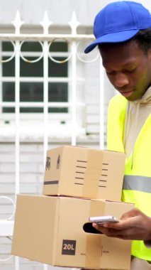 Afrikalı teslimatçı bir evin girişine elinde bazı paketler ile geliyor.