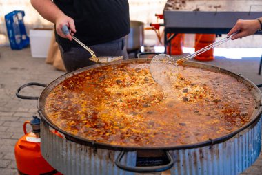 Bir adam büyük bir tencerede yemek pişiriyor. Tencere kırmızı sosla dolu ve adam karıştırmak için kaşık kullanıyor.