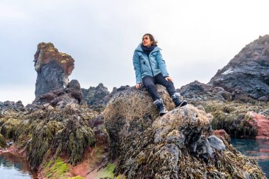 İzlanda 'daki Djupalonssandur plajında kayalıklarda oturan bir kadın yürüyüşçünün portresi