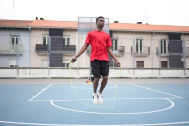 Spor kıyafetleri giyen genç Afrikalı Amerikalı bir basketbol sahasında ip atlıyor.