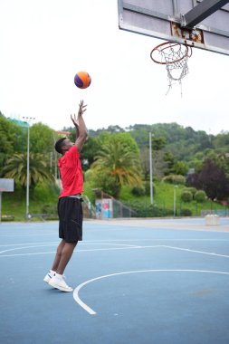 Açık hava sporları sahasında serbest atış talimi yapan Afrikalı bir basketbolcunun dikey yan görüntüsü