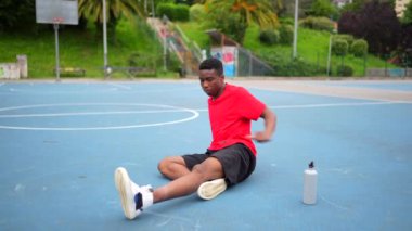 Afrikalı bir Amerikalı basketbolcu açık hava sahasında dinleniyor.