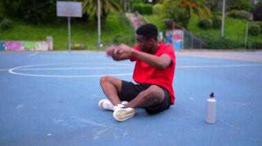 Afrikalı bir Amerikalı basketbolcu açık hava sahasında dinleniyor.