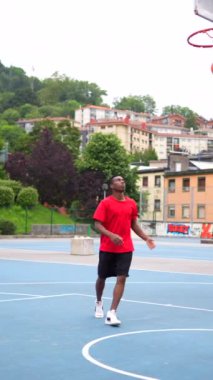 Açık hava mavi basketbol sahasında top atan bir basketbolcunun dikey videosu.