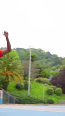 Açık hava mavi basketbol sahasında top atan bir basketbolcunun dikey videosu.