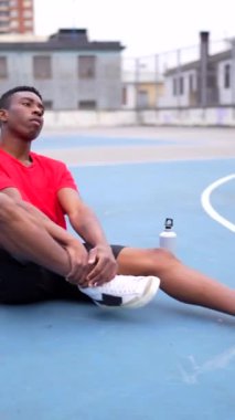 Açık bir sahada oturan Afrikalı Amerikalı bir basketbolcunun dikey portresi.