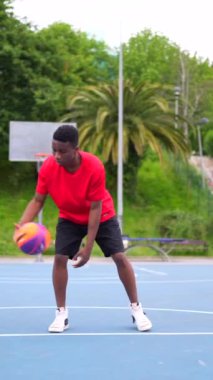 Açık hava tesislerinde antrenman yapan Afrikalı Amerikalı bir basketbolcunun dikey videosu.