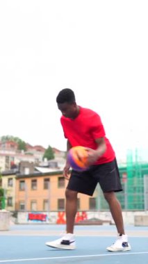 Açık havada top süren Afrikalı bir genç basketbolcunun dikey videosu.