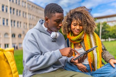 Üniversite kampüsünün dışında oturmuş tablet kullanan gülümseyen çok ırklı genç çift.