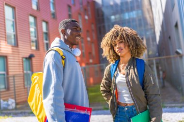 Üniversitenin dışındaki çok ırklı havalı öğrenciler ellerinde not defterleriyle sırt çantası taşıyorlar.