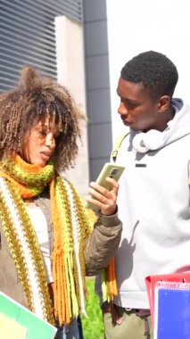 İki çok ırklı Latin ve Afrikalı öğrenci üniversite kampüsünde yürürken cep telefonu kullanıyor.