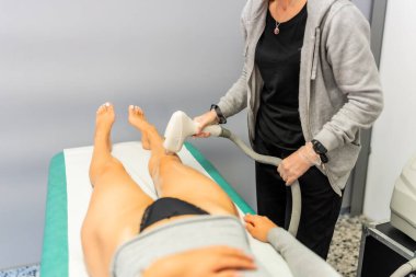 Estetisyen bir tüy dökücü tutuyor ve kadının bacakları üzerinde kullanıyor.