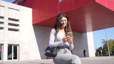 Şehrin ticari ve endüstriyel alanındaki bir bankta oturan kadın cep telefonu kullanıyor.