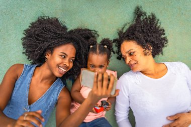 Parkta uzanan cep telefonunu izleyen üç Afrikalı çok nesilli kadının en iyi görüntüsü.