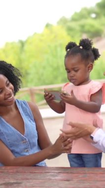 Annesi ve büyükannesi arka planda konuşurken Afrikalı şirin bir kızın parkta cep telefonu kullanması.