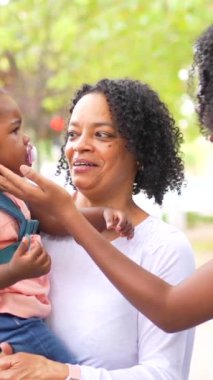 Üç kuşak Afrikalı kadın aile halka açık bir parkta bir kızı ve oyuncakları taşıyor.